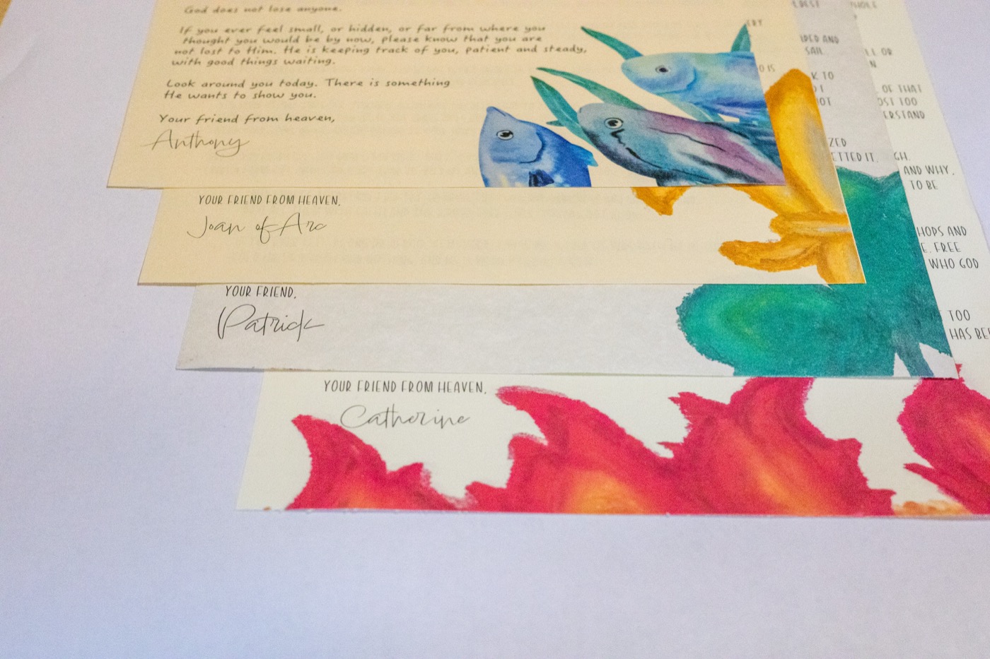 Four saint letters fanned out, signed by Anthony, Joan of Arc, Patrick, and Catherine — each ends 'Your friend from heaven'