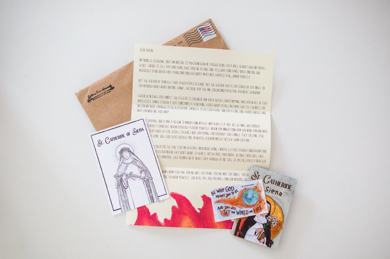 Letters from Heaven monthly subscription — saint letter, prayer card, sticker, and zine spread on a wooden table